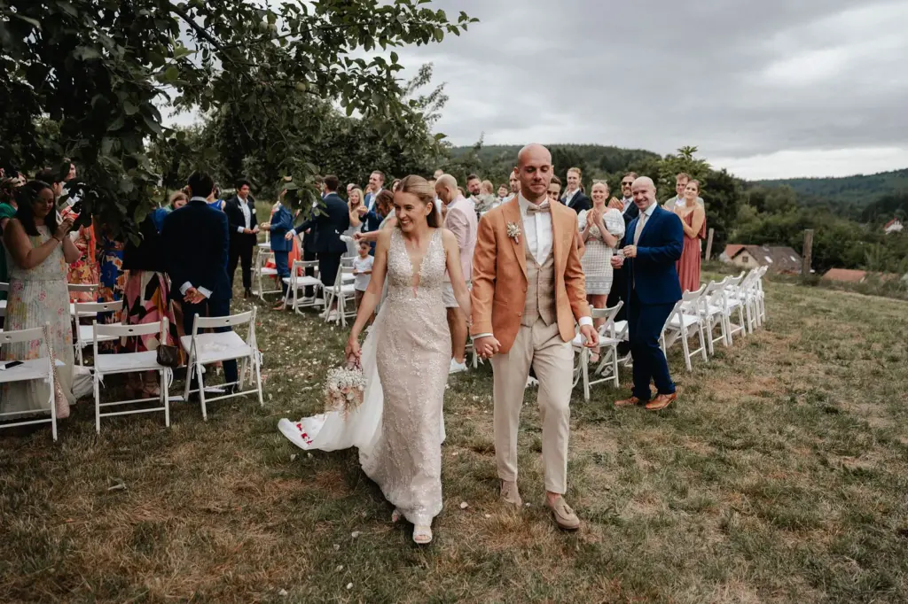 Auszug nach der freien Trauung: Brautpaar geht Hand in Hand durch die Reihen, Gäste applaudieren – Spessarthof, Aura im Sinngrund (bei Mittelsinn, Bayern).