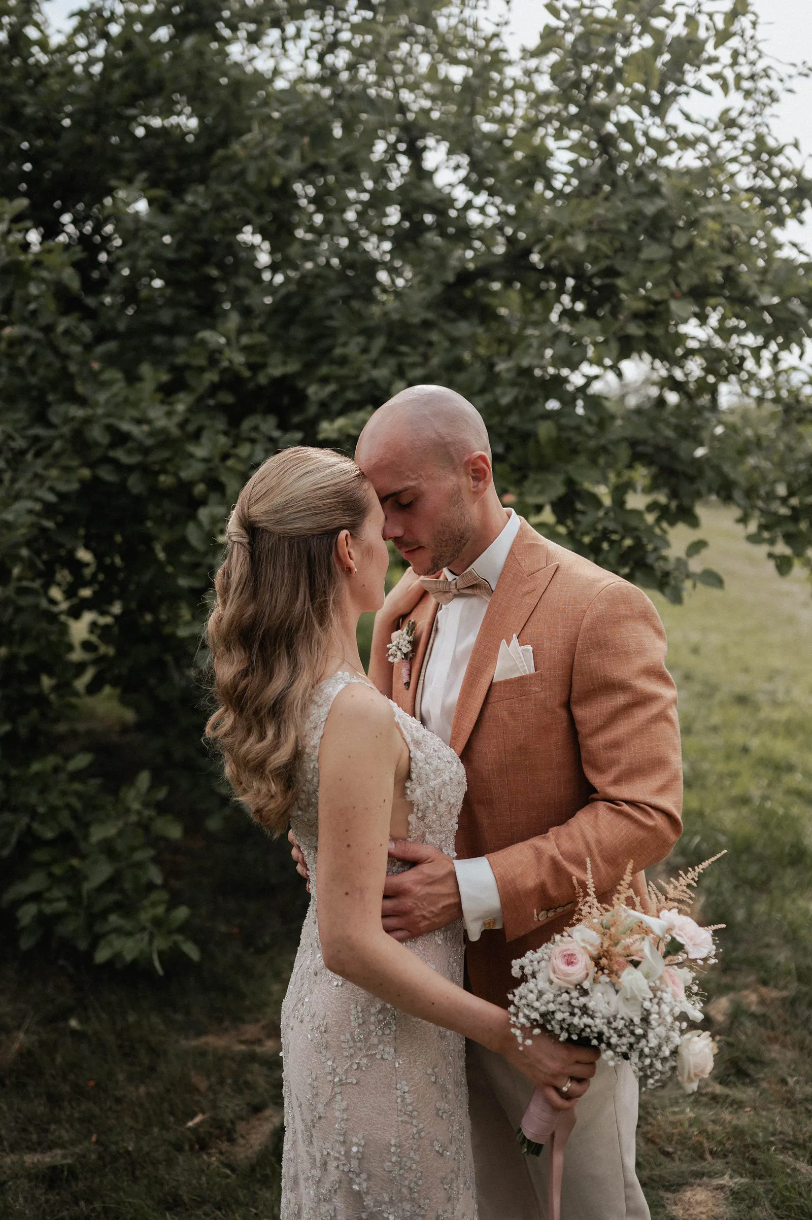 Inniger Moment beim Brautpaar-Portrait: Braut und Bräutigam stehen eng beieinander, sie hält den Brautstrauß – Spessarthof, Aura im Sinngrund (bei Obersinn, Bayern).