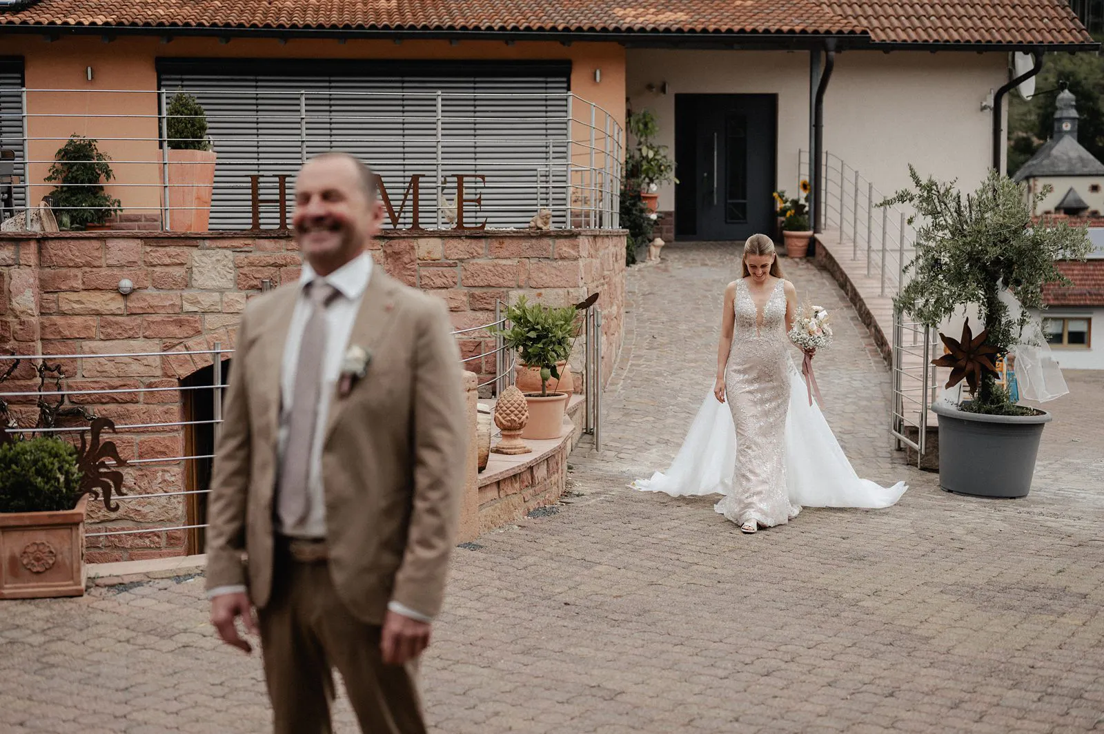 First Look mit dem Vater: Braut nähert sich von hinten, der Vater steht lächelnd im Vordergrund – Spessarthof, Aura im Sinngrund (Unterfranken, Bayern).