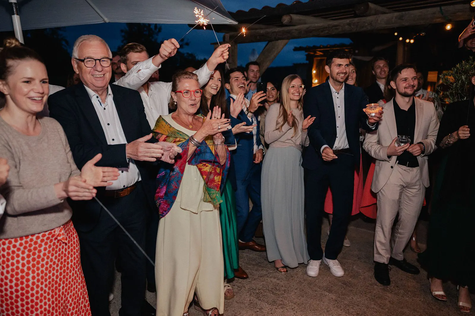 Gäste jubeln und halten Wunderkerzen in die Luft bei der Hochzeitsparty am Abend – Spessarthof, Aura im Sinngrund, Bayern (Naturpark Bayerischer Spessart).