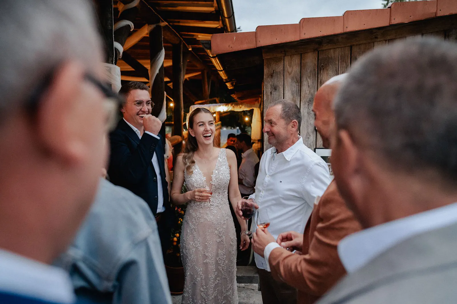 Die Braut lacht mit Gästen beim Sektempfang am Abend vor der Scheune – Spessarthof, Aura im Sinngrund, Bayern (Naturpark Bayerischer Spessart).