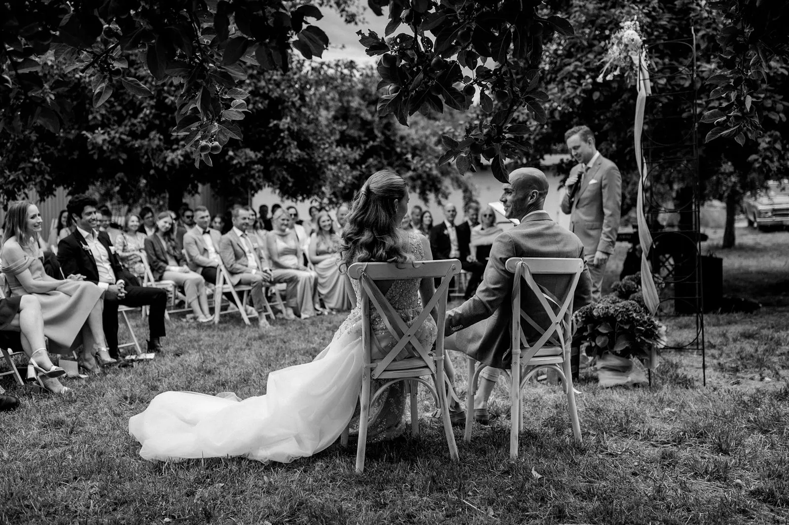 Brautpaar sitzt bei der freien Trauung vor den Gästen im Obstgarten beim Spessarthof.